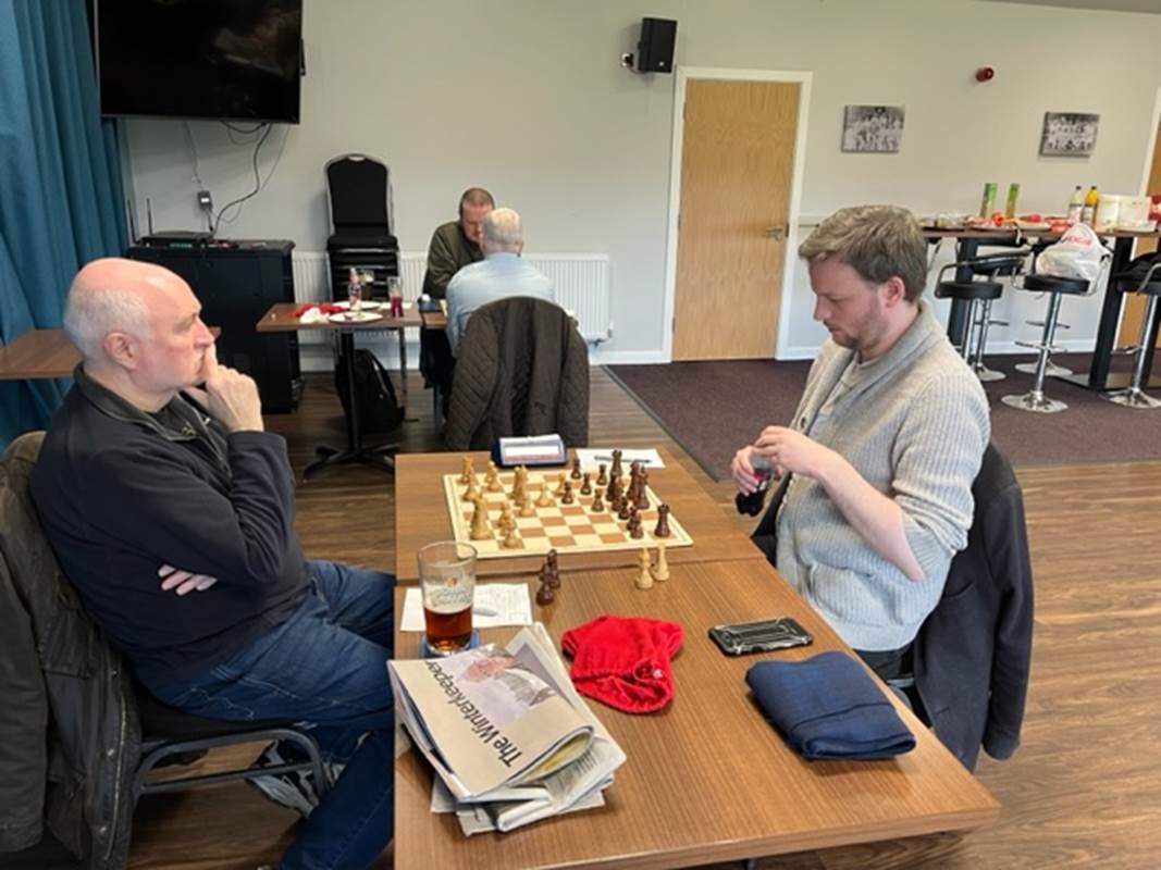 Two men sitting at a table with chess board and a glass of beer

Description automatically generated